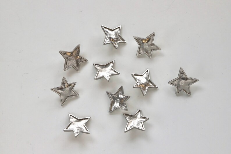 Puede incluir: Diez adornos de metal en forma de estrella plateados con textura martillada.