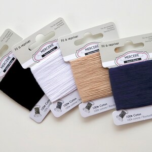 May include: Four spools of 100% cotton thread in black, white, beige, and navy blue. Each spool is labelled "Fil à repriser" and "Mercerie Saint-Pierre".