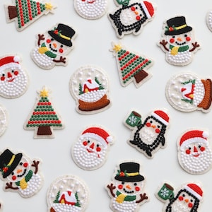 May include: A selection of embroidered iron-on patches featuring Christmas themes, including snowmen, Father Christmas, penguins, and Christmas trees. The patches are made with white, red, green, and black thread.