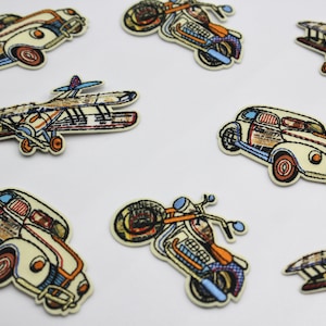 May include: A set of nine iron-on patches featuring vintage-style illustrations of cars, motorcycles, and aeroplanes. The patches are in various colours, including red, blue, yellow, and white.