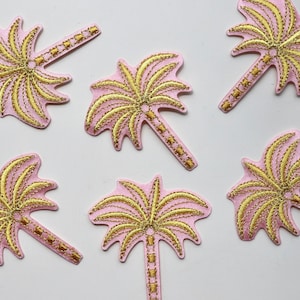 Puede incluir: Seis parches termoadhesivos de color rosa en forma de palmera con bordados dorados. Las palmeras tienen un dise&ntilde;o sencillo con un tronco y hojas.