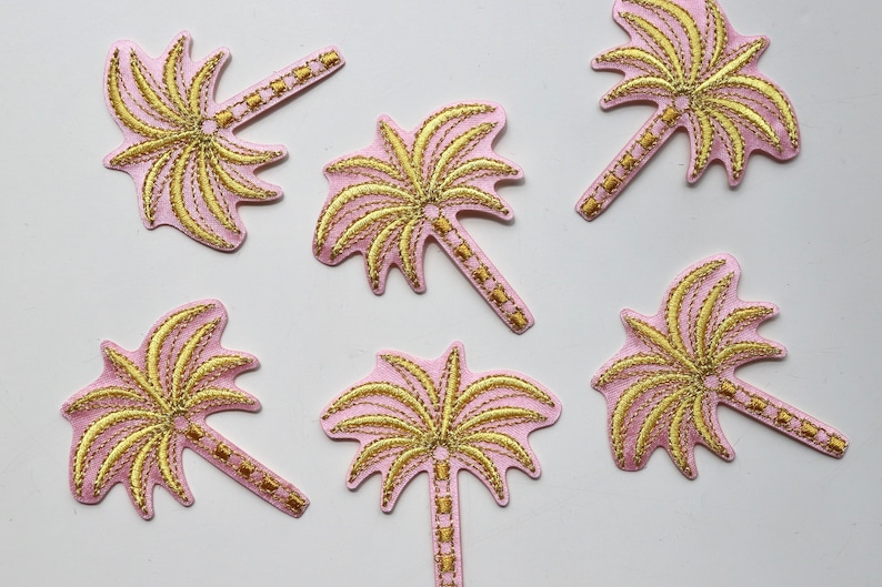 Puede incluir: Seis parches termoadhesivos de color rosa en forma de palmera con bordados dorados. Las palmeras tienen un dise&ntilde;o sencillo con un tronco y hojas.