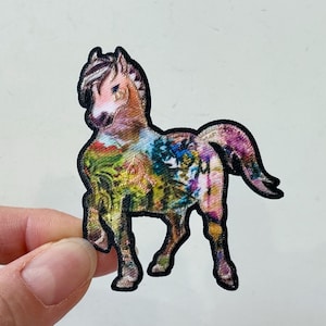May include: A colourful horse patch with a black outline. The horse is standing on all four legs and has a long tail. The patch is made of fabric and has a detailed design.