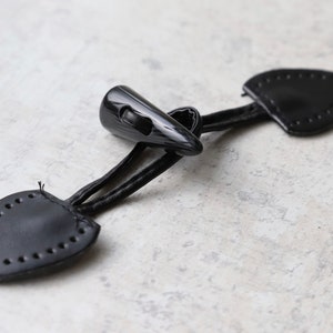 May include: Black leather toggle closure with a black plastic hook. The toggle is designed to be used on clothing.