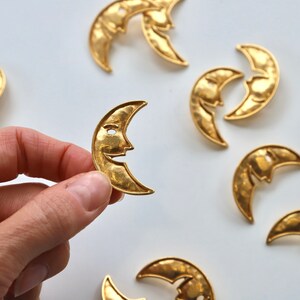 Puede incluir: Una colecci&oacute;n de ocho dijes de metal dorado en forma de media luna con un dise&ntilde;o de cara. Los dijes est&aacute;n martillados para un aspecto texturizado.