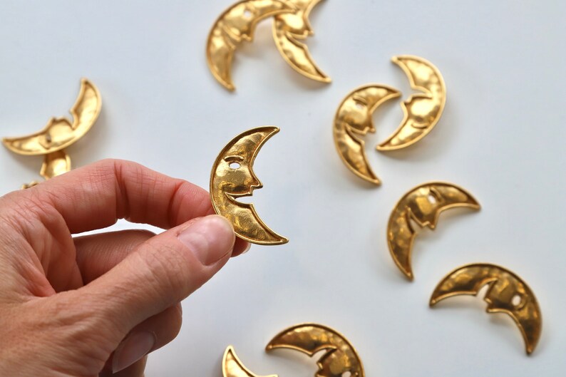 Puede incluir: Una colecci&oacute;n de ocho dijes de metal dorado en forma de media luna con un dise&ntilde;o de cara. Los dijes est&aacute;n martillados para un aspecto texturizado.