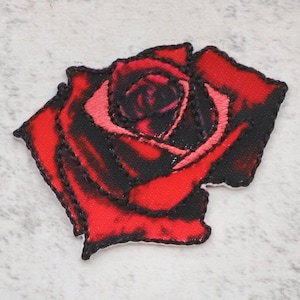 May include: An embroidered patch featuring a red rose with black stitching. The rose is in full bloom with a dark red centre and light red petals.