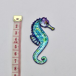 May include: A blue and green iridescent sequin seahorse applique patch. The seahorse is approximately 5 cm tall.