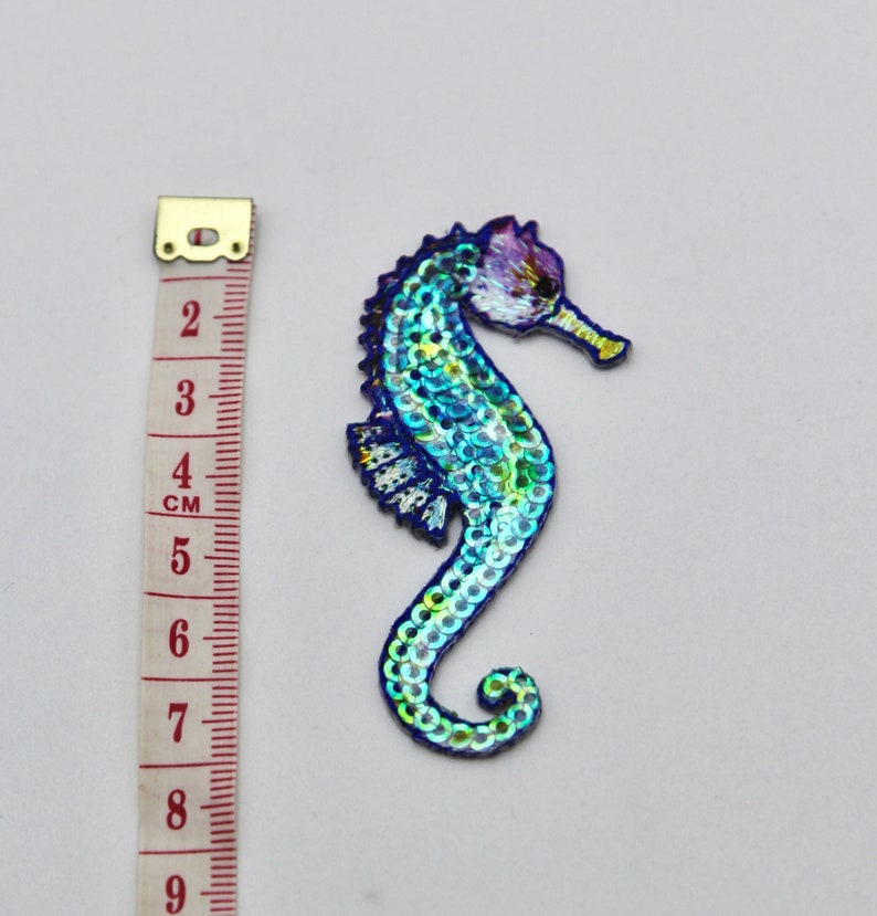 May include: A blue and green iridescent sequin seahorse applique patch. The seahorse is approximately 5 cm tall.