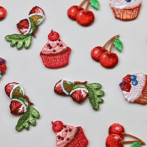 May include: Assortment of embroidered iron-on patches featuring cupcakes, cherries, and acorns. The patches are in shades of red, green, and white.