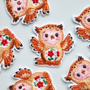 May include: Six embroidered iron-on patches featuring a cartoon owl with a floral design in shades of orange, pink, and white.