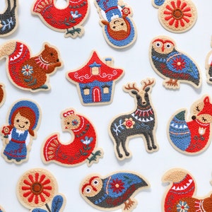 May include: A collection of embroidered iron-on patches featuring various woodland creatures, houses, and flowers. The patches are in shades of red, blue, and brown with intricate details.