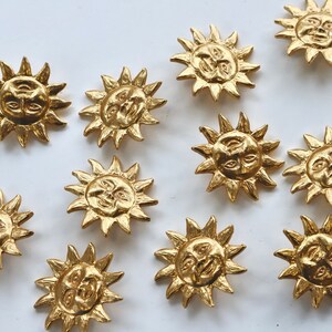Puede incluir: Doce botones dorados en forma de sol con un dise&ntilde;o de cara. Cada bot&oacute;n tiene una cara en relieve con dos ojos, una nariz y una boca.