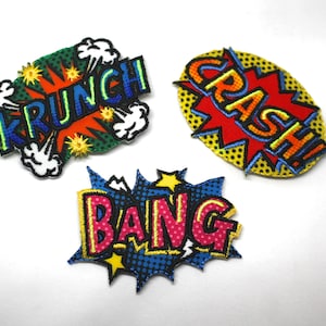 May include: Three colourful embroidered iron-on patches with comic book style speech bubbles. The patches say "Krunch", "Crash!" and "Bang".