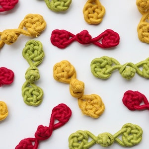 May include: Assortment of colourful fabric buttons in red, yellow and green. The buttons are tied in a knot and have a unique, decorative design.