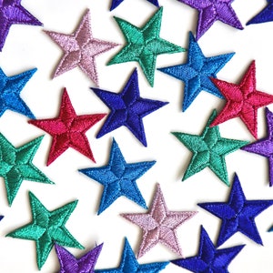 May include: Assortment of colourful star-shaped fabric patches in various shades of blue, green, purple, and red. The patches are perfect for adding a touch of whimsy to clothing, bags, or other crafts.