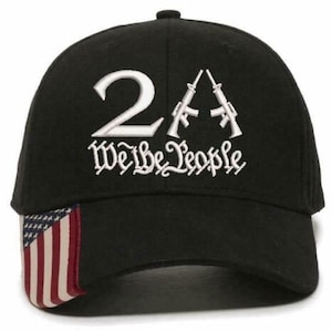 May include: Black baseball cap with white embroidered text and graphics. The text reads "2A We the People" with two rifles. The cap features an American flag design on the side.