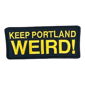 Op de afbeelding: Een rechthoekige zwarte patch met de woorden "KEEP PORTLAND WEIRD!" geborduurd in geel. De patch heeft een zwarte rand en is waarschijnlijk ontworpen om op kleding of accessoires te worden genaaid.