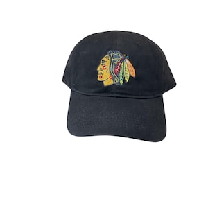 May include: Black baseball cap with an embroidered logo of a Native American head with feathers in red, white, black and green.