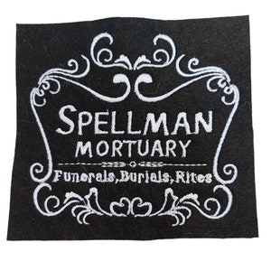 May include: Black and white embroidered patch with the text "SPELLMAN MORTUARY Funerals, Burials, Rites" in a decorative frame.