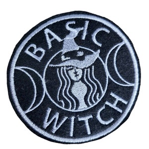 May include: A black and white embroidered patch with the text "Basic Witch" in a circle. The center of the circle features a witch with a pointed hat and long hair.