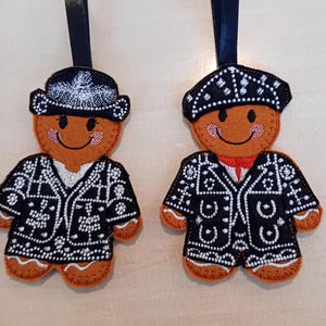 May include: Two gingerbread person ornaments with black and white patterned jackets and hats. The gingerbread people are smiling and have red cheeks.
