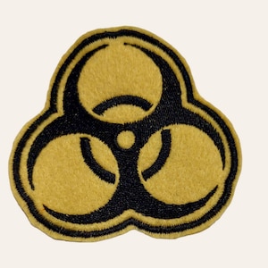 May include: A black and yellow biohazard symbol embroidered patch. The symbol is a stylized three-leaf clover with a circle in the center.