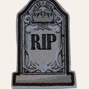 May include: A grey tombstone with black embroidery. The tombstone has a decorative design and the word "RIP" in black lettering.