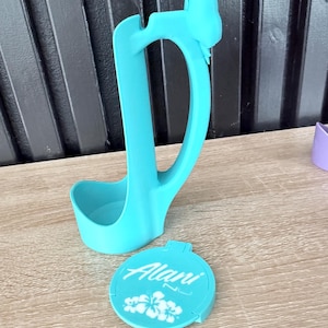 Puede incluir: Un cuchar&oacute;n azul claro con un asa en forma de lazo y una tapa a juego. La tapa es redonda y presenta el nombre "Alani" en escritura blanca, junto con dise&ntilde;os florales blancos. El cuchar&oacute;n y la tapa son de pl&aacute;stico.