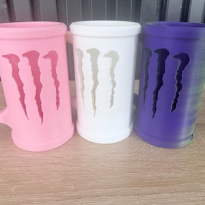 May include: Three colorful mugs with a distinctive design. The mugs are in pink, white, and purple. Each mug features a cut-out design resembling claw marks. The pink mug has a handle, while the others are cylindrical.