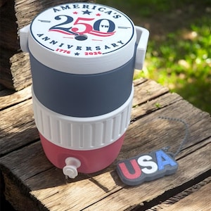 May include: A water cooler in red, white, and blue, featuring the text "America's 250th Anniversary 1776-2026". It has a white handle and a "USA" tag. The cooler is likely to hold several liters of liquid.