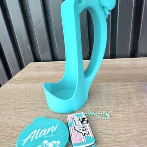 Puede incluir: Un portavasos de pl&aacute;stico azul claro con un detalle de lazo, un espejo compacto y un llavero. El espejo y el llavero tienen la palabra "Alani". El llavero tiene un dise&ntilde;o de rayas rosas y azules.