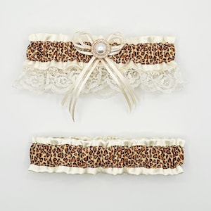May include: Two-piece set of bridal garters. The top garter features a leopard print band with ivory lace trim and a pearl-centered bow. The bottom garter has a matching leopard print band and ivory trim. Both are set against a white background.