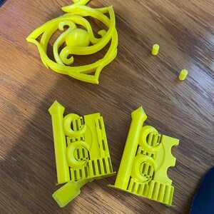 May include: A set of yellow 3D printed plastic pieces, including a decorative piece with a swirl design and two pieces with a repeating pattern of circles and lines.