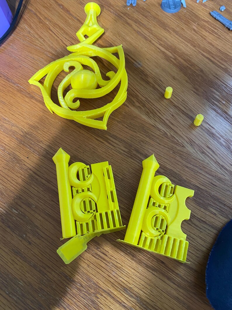 May include: A set of yellow 3D printed plastic pieces, including a decorative piece with a swirl design and two pieces with a repeating pattern of circles and lines.
