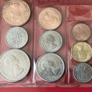May include: A selection of vintage British coins, including various denominations, presented in a clear plastic holder. The coins feature profiles and inscriptions, with a mix of silver, bronze, and gold tones. The coins are from the reign of Elizabeth II.