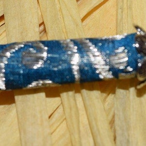 May include: A small, silver-colored, decorative scroll with a blue fabric covering and silver beads at each end.