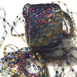 May include: A tightly wound spool of decorative ribbon with a woven pattern. The ribbon is primarily black with colorful accents of pink, blue, yellow, and green. Strands of the ribbon extend from the spool, creating a textured effect.