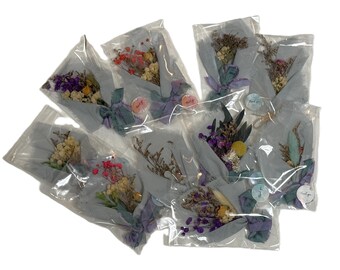 May include: A collection of small, dried flower bouquets wrapped in light gray paper and clear plastic. Each bouquet is tied with a ribbon and includes a small sticker. The flowers are various colors, including purple, yellow, and red.