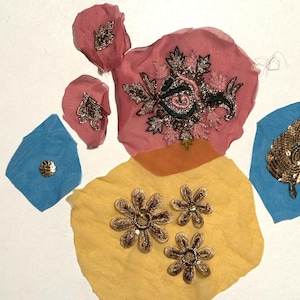 May include: An assortment of fabric pieces in pink, yellow, and blue, adorned with gold and silver embellishments. The pieces include floral and leaf shapes, and a central pink piece with intricate embroidery.