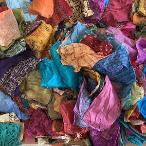 May include: A pile of colorful fabric scraps in various shades of blue, purple, pink, orange, and green. The fabric is made of silk and has a variety of patterns, including floral, paisley, and geometric designs.