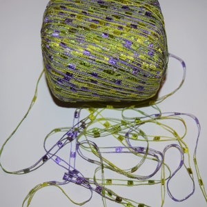 May include: A skein of green and purple yarn with a glittery finish. The yarn is made of thin strands with small squares woven into the fabric.