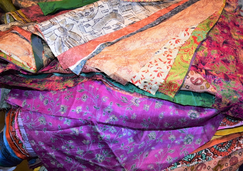 May include: A pile of colorful fabric scraps with various floral and paisley patterns. The fabrics are in shades of pink, purple, orange, green, and blue.