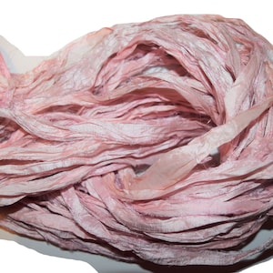 May include: A bundle of pink silk ribbon, with a slightly iridescent sheen, is arranged in a loose, flowing pile.