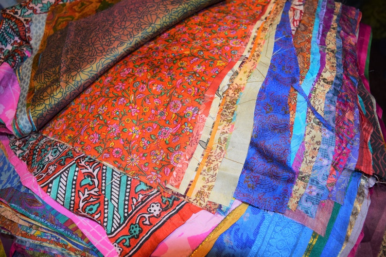 May include: A pile of colorful fabric scraps in various patterns and textures, including floral, paisley, and geometric designs. The fabrics are arranged in a layered and overlapping fashion, creating a visually appealing and textured composition.