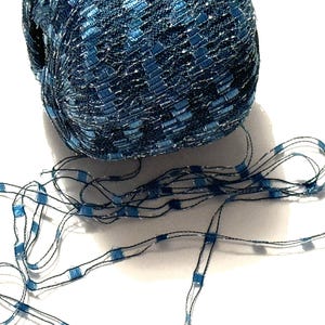 May include: A skein of blue and silver yarn with a metallic sheen. The yarn is made of a fine, delicate thread and has a loose, open weave.