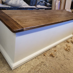 May include: A white wooden storage bench with a dark brown wood top. The bench has a decorative trim around the bottom edge.