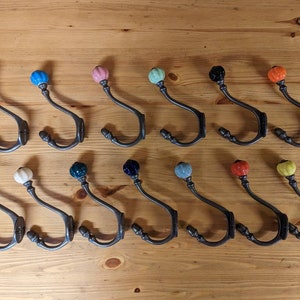 May include: A set of 14 ceramic knob hooks in various colours, including pink, blue, green, yellow, orange, and black. The hooks are made of metal and have a simple, elegant design.