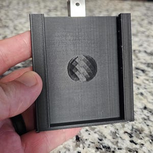 May include: A black plastic badge holder with a metal clip and a circular, textured design in the center.