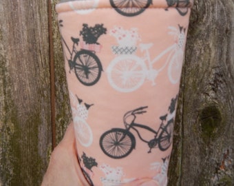 May include: A pink and white reusable cup sleeve with a black and white bicycle pattern. The sleeve has a black and white bicycle with a basket of flowers on it.